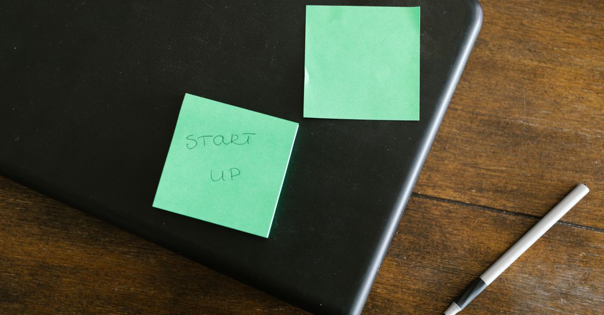 A laptop with green sticky notes and a pen on a wooden desk, symbolizing startup planning.