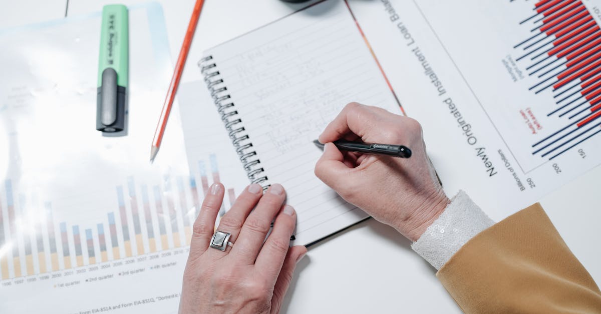 Close-up of hands writing notes in a notebook with charts and graphs on a desk.