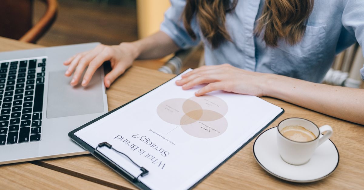 A person reviews a brand strategy document on a clipboard while using a laptop in an office setting.