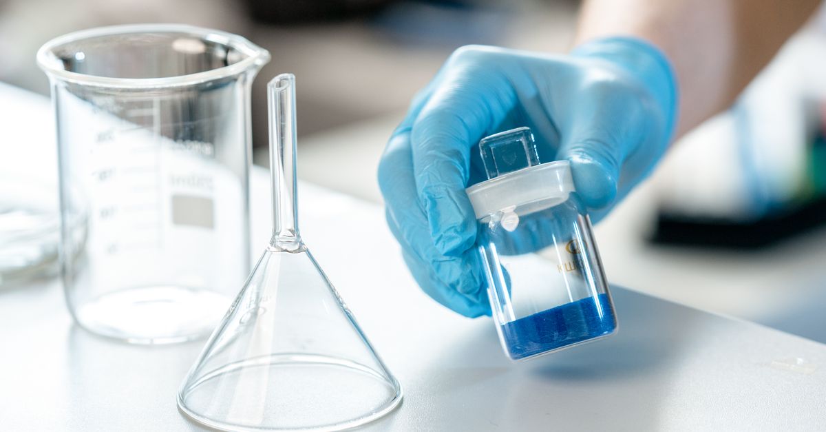 Scientist holding vial with blue liquid next to beaker and funnel in lab.