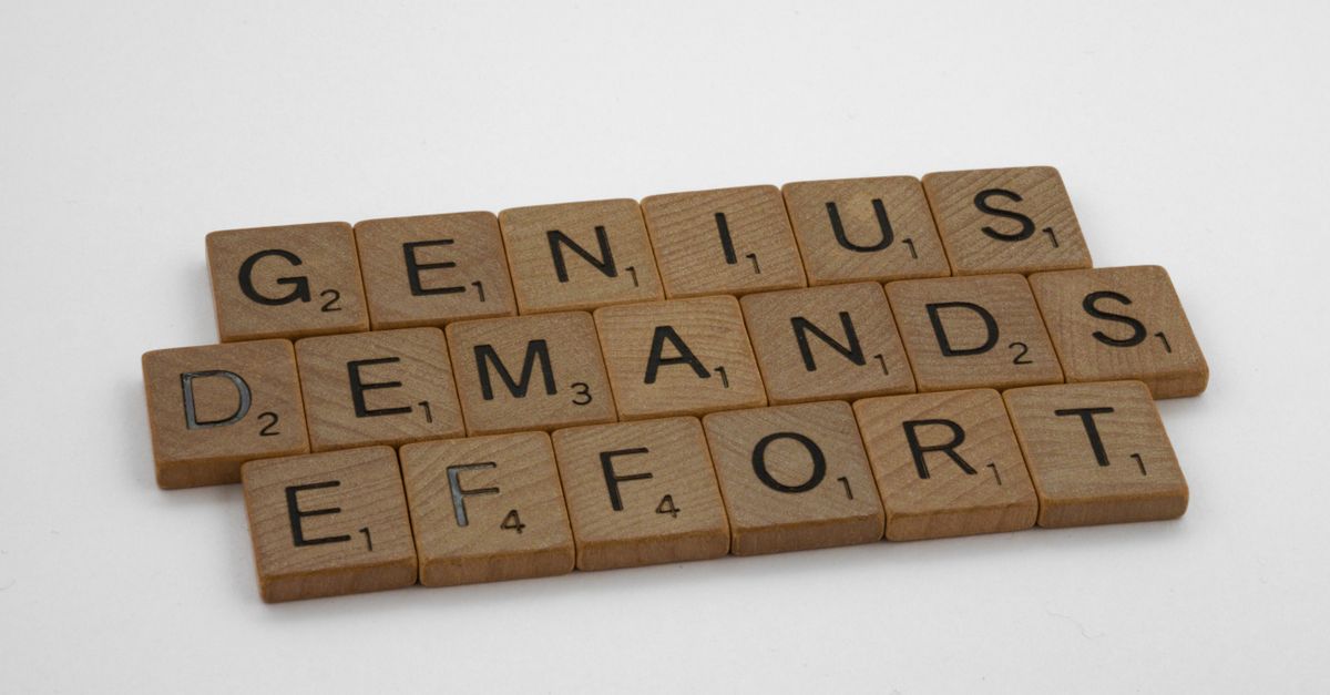 Scrabble tiles spelling 'Genius Demands Effort' on white surface, highlighting creativity and persistence.