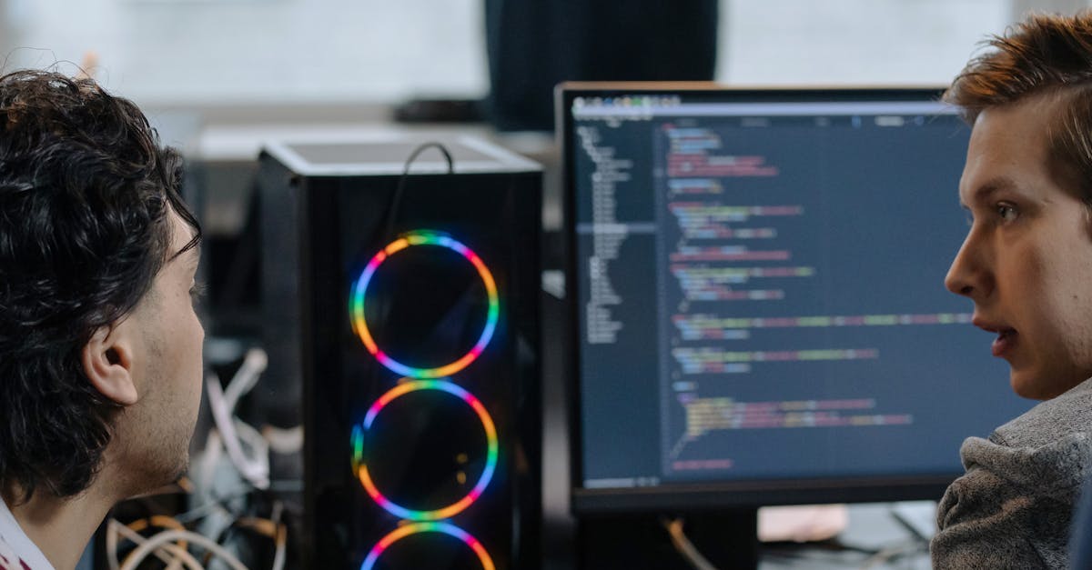 Two programmers discussing code on a monitor in a tech workspace, focusing on collaboration.