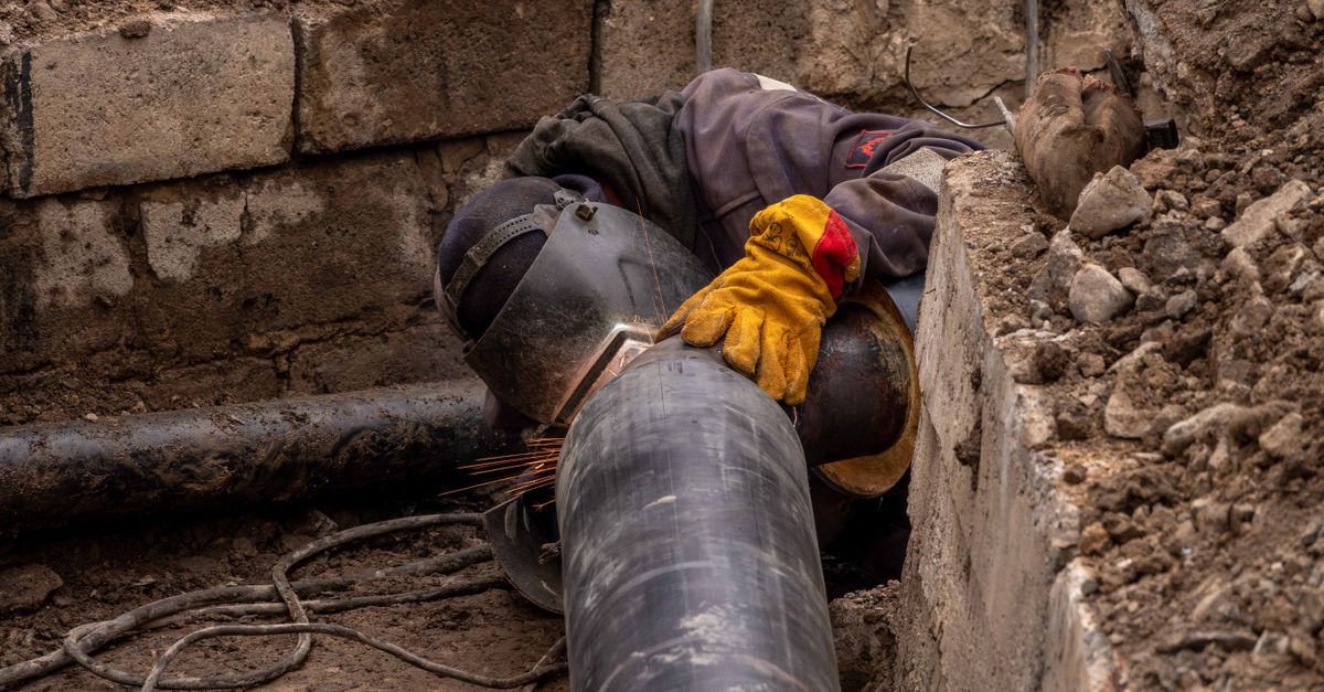 A worker welds a pipe in an urban trench, showcasing industrial construction work.