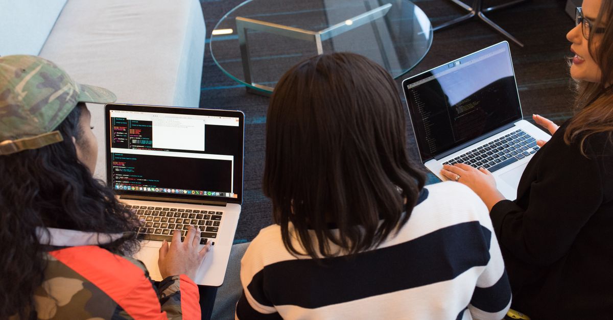 Three women working on laptops in a stylish office, focused on a collaborative project.