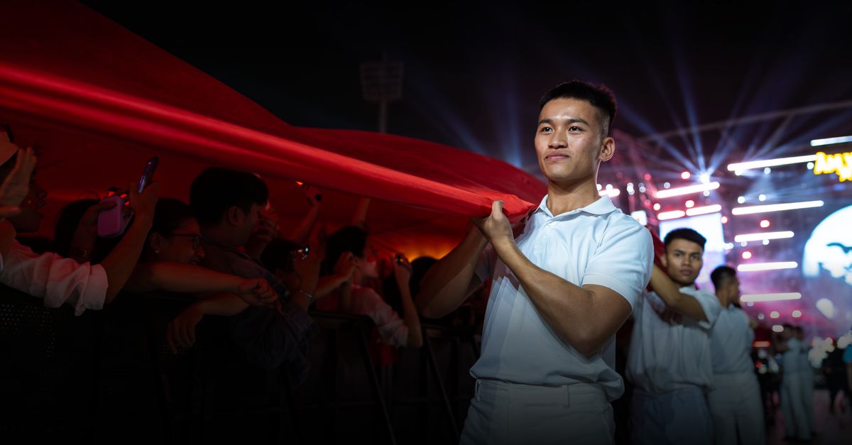 Proud young man holding a large flag at a vibrant nighttime event with lights.
