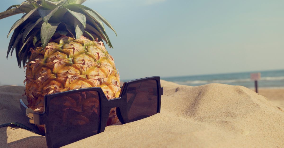A pineapple wearing sunglasses enjoys a sunny day on the beach, epitomizing tropical vibes.