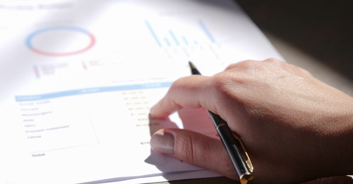 A close-up view of a hand holding a pen and examining financial charts on paper.