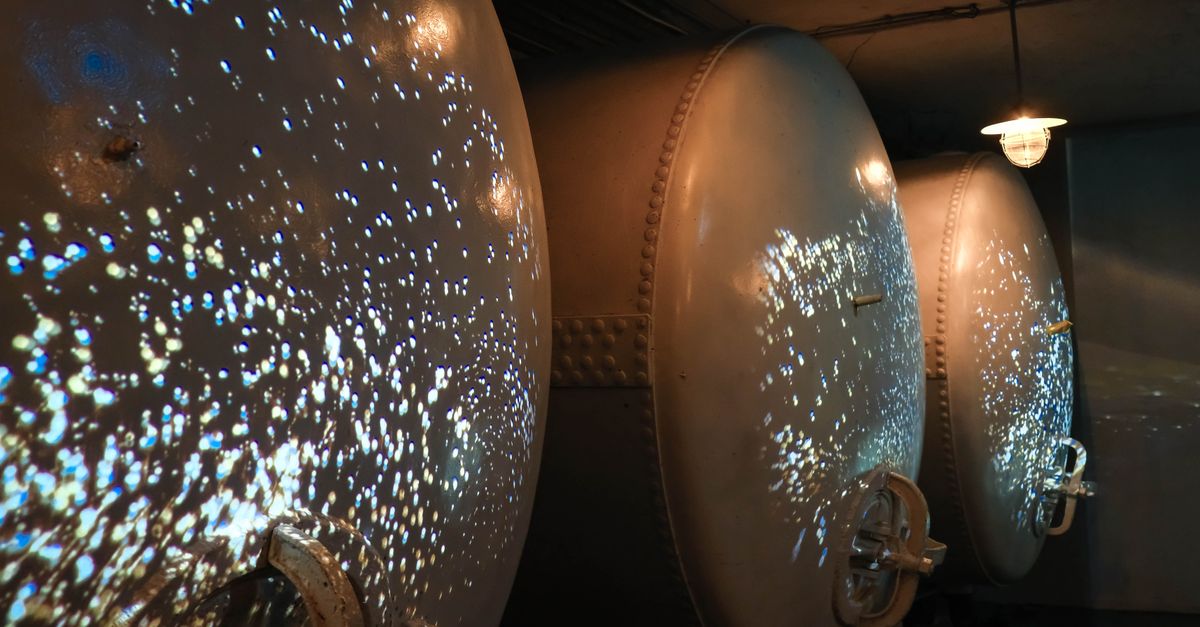 Dimly lit industrial wine fermentation tanks with unique light reflections creating a futuristic atmosphere.