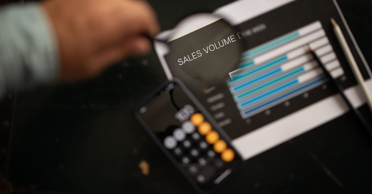 A focused examination of sales volume data using a magnifying glass and calculator.