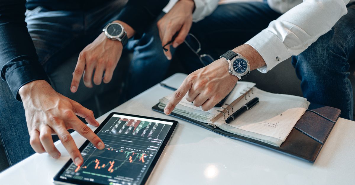 Two businessmen discussing financial data on a tablet during a meeting.