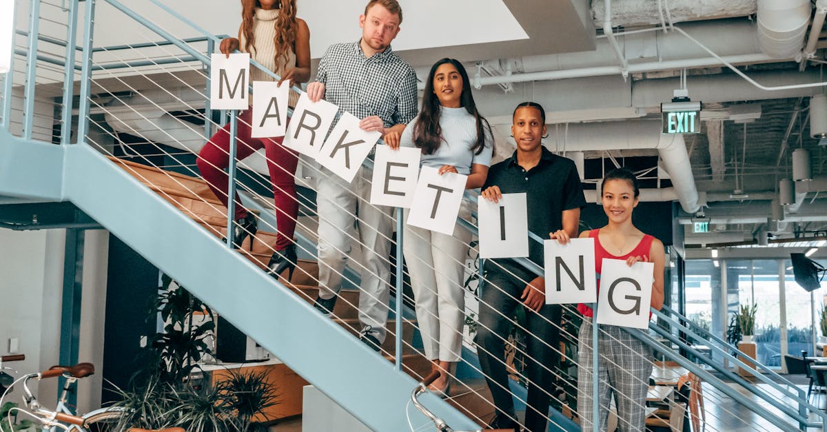 A diverse team of coworkers in an office holding a marketing sign on a staircase, smiling and happy.