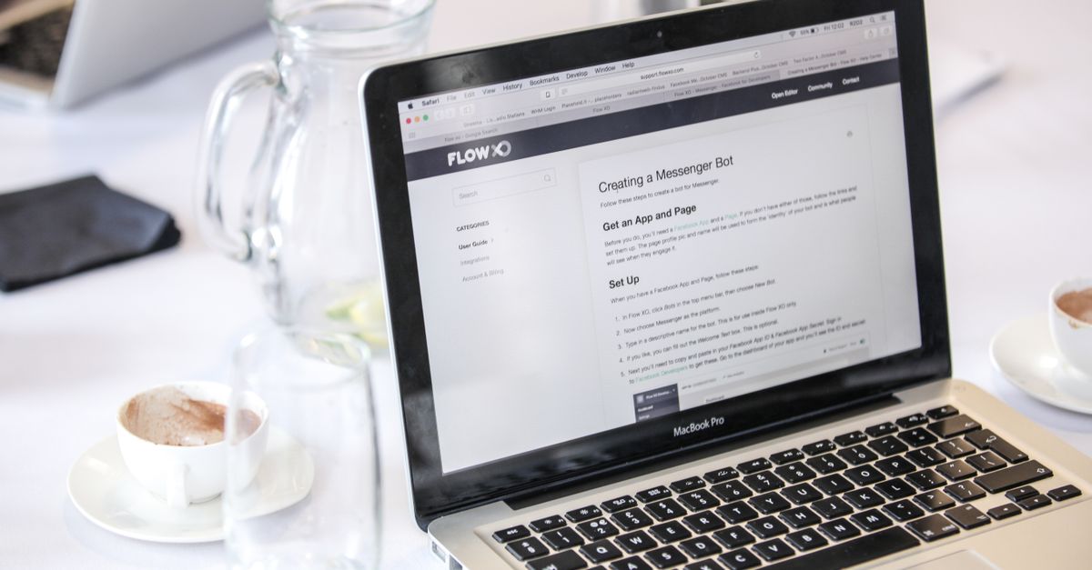 Close-up of a MacBook Pro displaying a webpage, with coffee cups and water pitcher on a table.