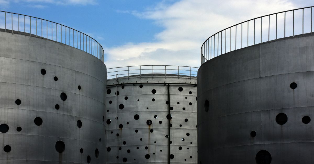 Large metal silos with perforated design standing under a clear blue sky in an industrial setting.