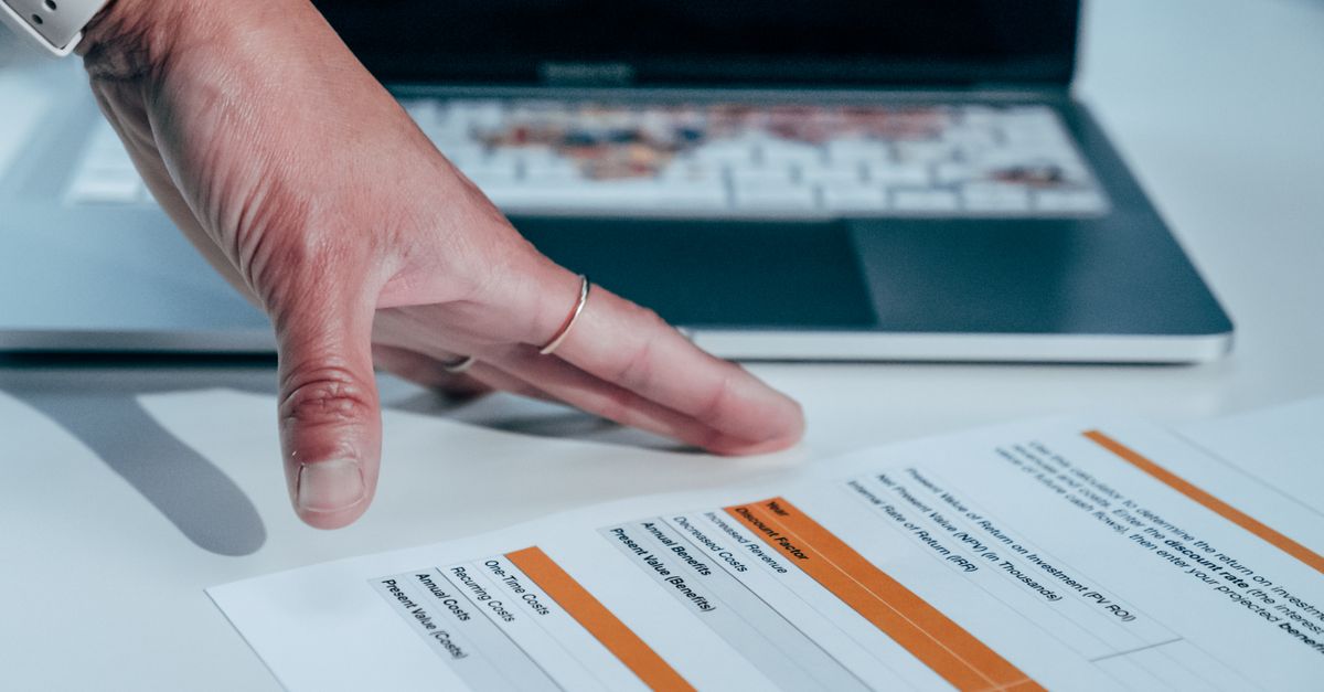 Close-up of a hand reviewing a financial report on a laptop, indicating focus on business analysis.