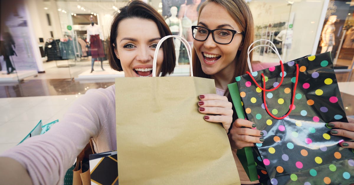 Two women smiling with shopping bags in a mall environment.
