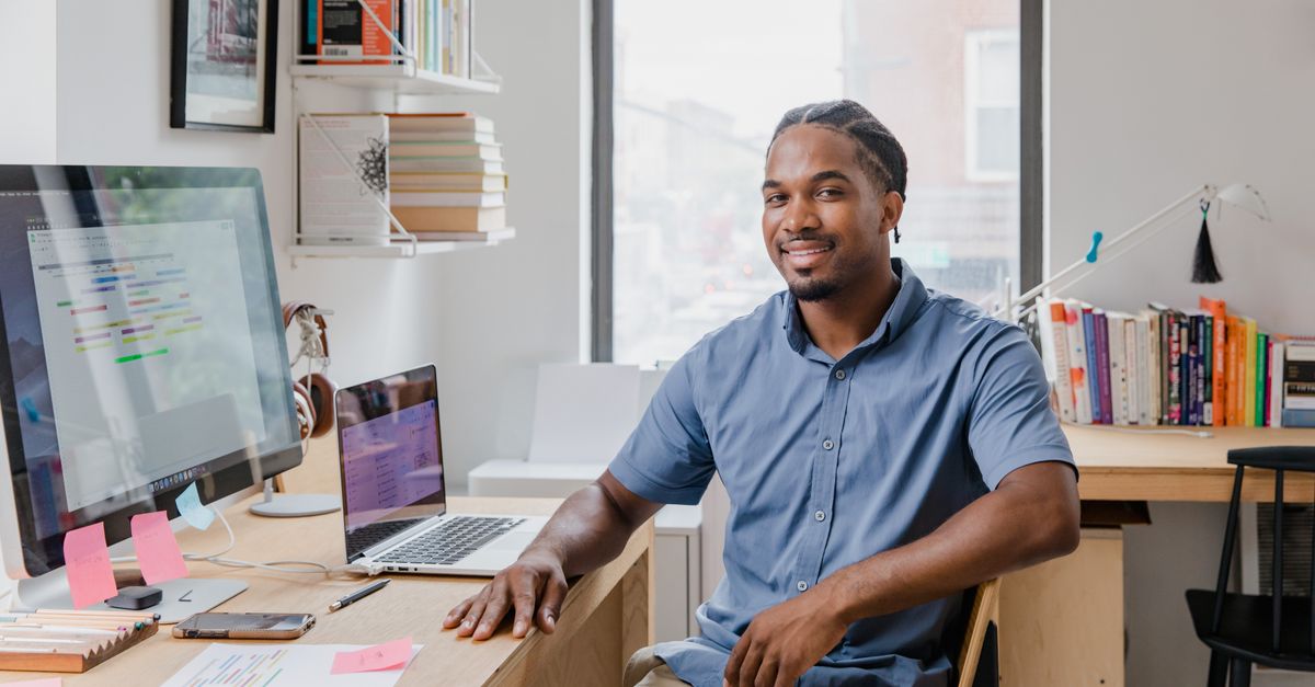 Confident professional man with a welcoming smile sitting at a desk in a contemporary office setting.