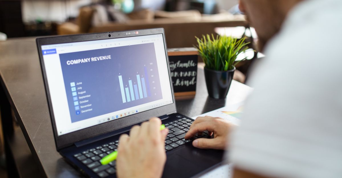 Man using a laptop to analyze company revenue data with graph charts in office setting.