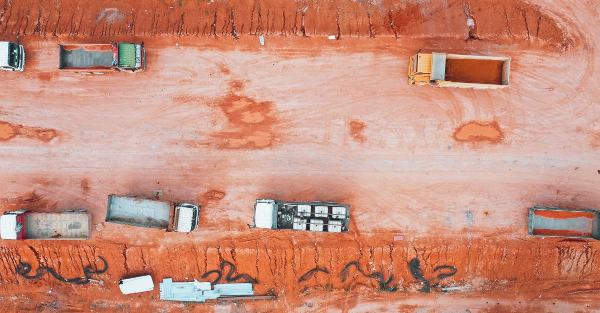 Aerial view of trucks on a construction site with orange soil and earthworks.