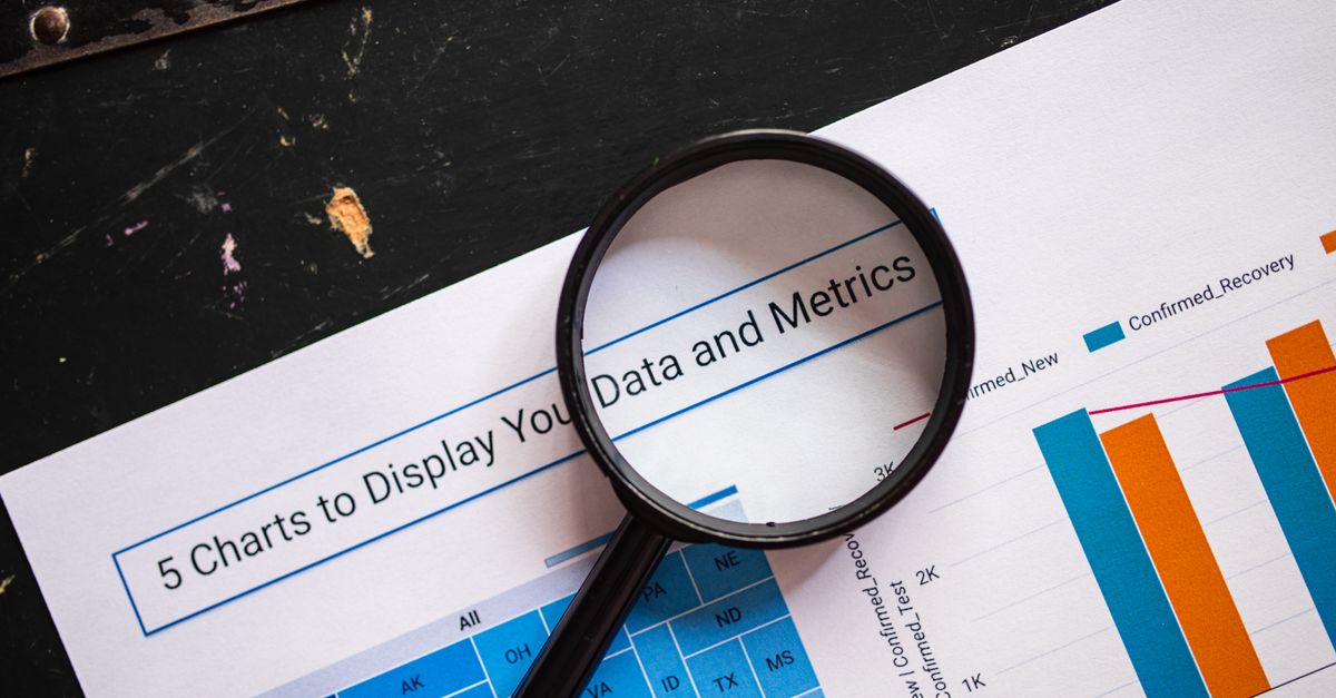 Close-up of a magnifying glass over financial data charts and metrics on printed paper.