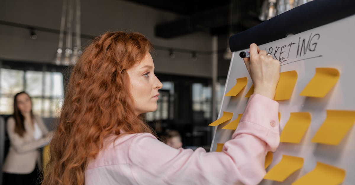 Red-haired woman writing on a whiteboard with sticky notes in a modern office setting.