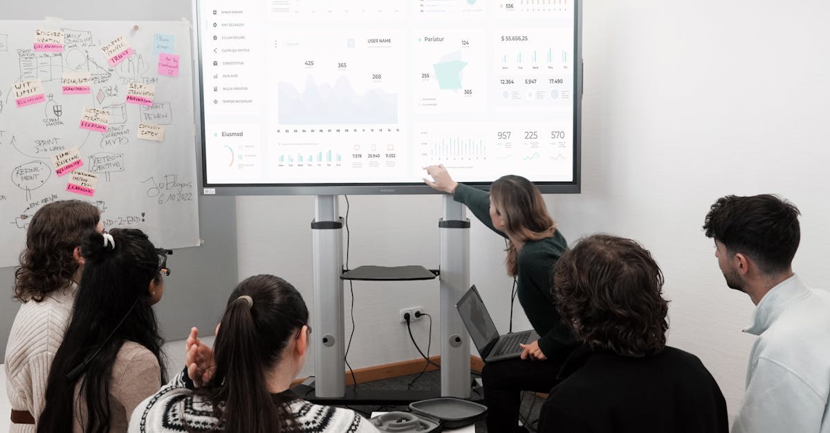 Group of professionals engaged in a business presentation examining charts on a large screen.