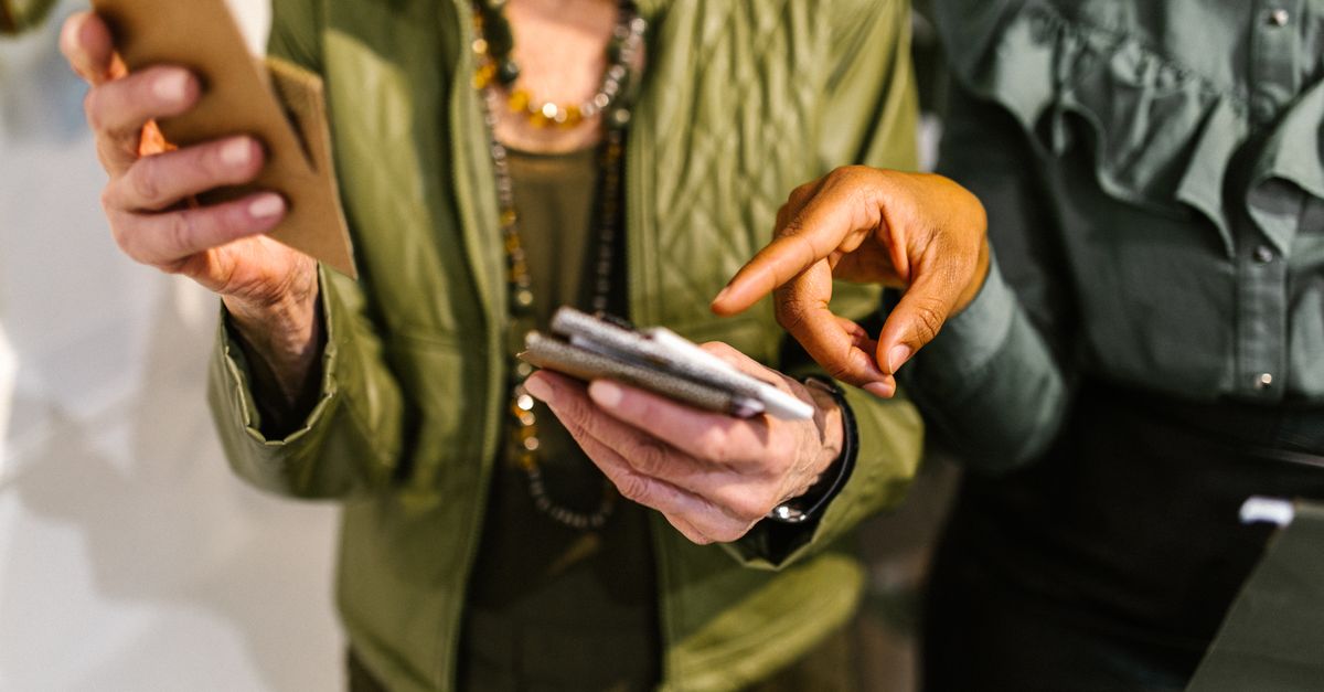 Two businesswomen collaborating using mobile phones in a modern office setting.