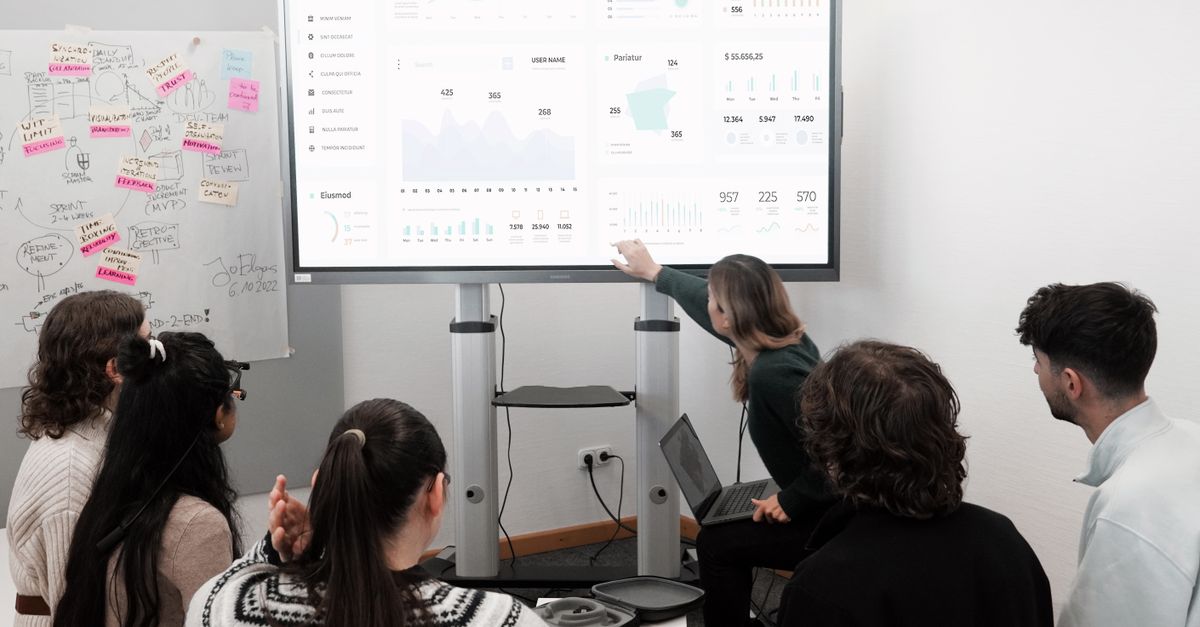 Group of professionals engaged in a business presentation examining charts on a large screen.