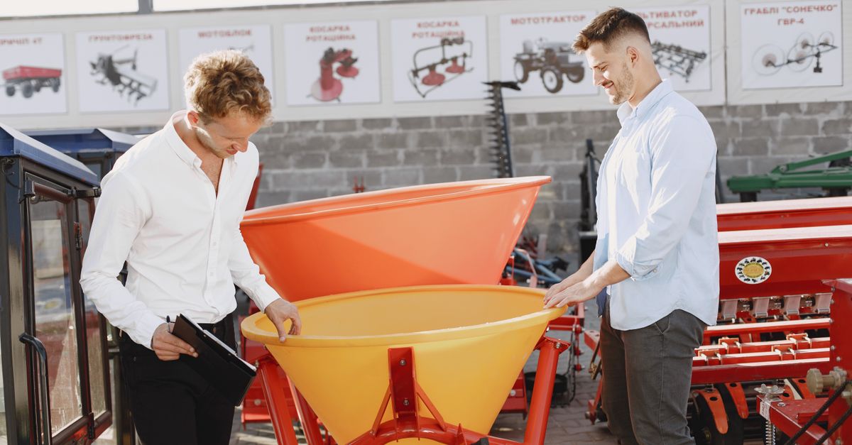 Two men examine agricultural equipment in an outdoor showroom, evaluating potential purchase.