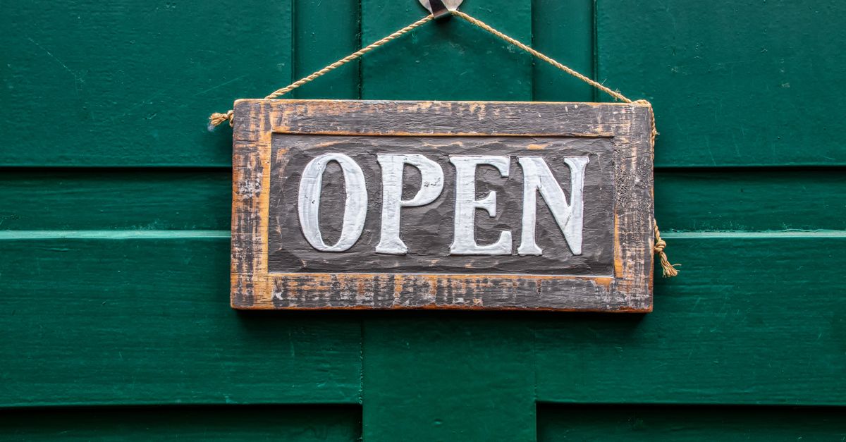 A vintage wooden open sign hanging on a rustic green door, symbolizing welcoming and accessibility.