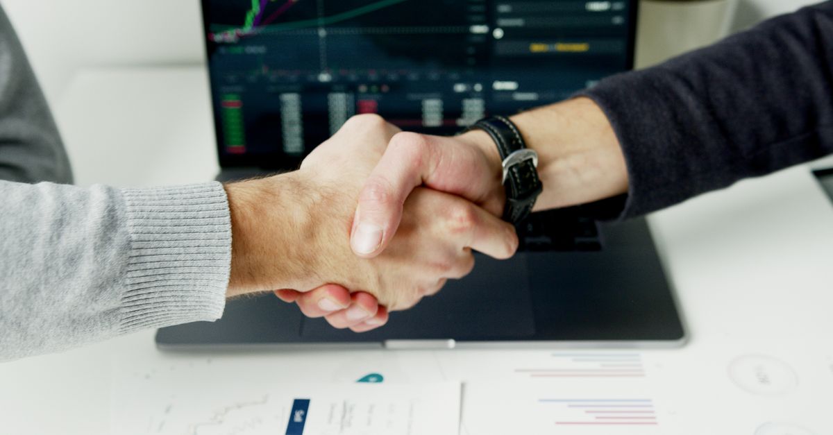 Close-up of a handshake with financial graphs on laptop screen, symbolizing a successful agreement.