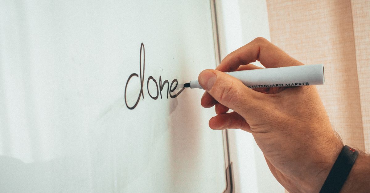 Crop unrecognizable male coach writing done word on whiteboard during presentation in light office