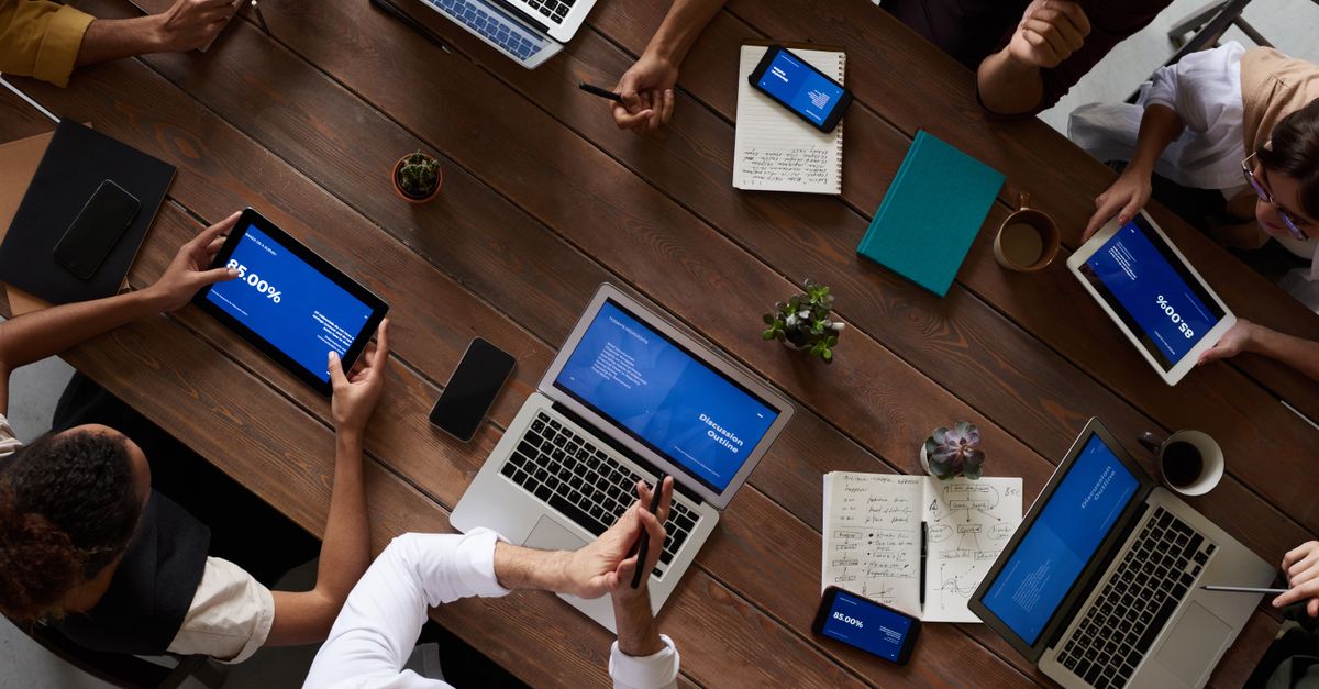 Overhead view of a diverse team discussing around a wooden table, using technology.