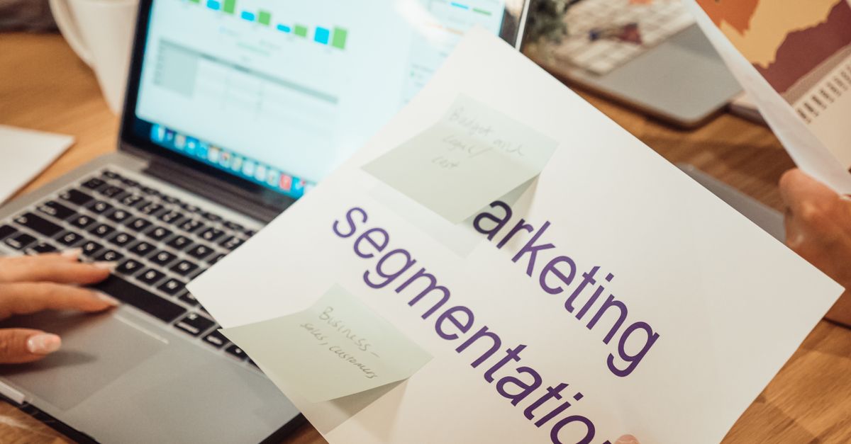 A modern workspace showing hands analyzing marketing data on a laptop and paper documents.