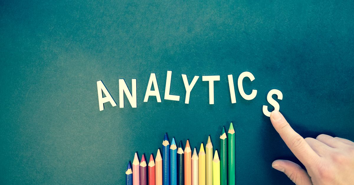 Colored pencils and letters spelling 'ANALYTICS' on a textured background with a hand.