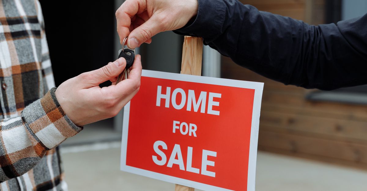 Close-up of a home for sale sign with people exchanging keys.
