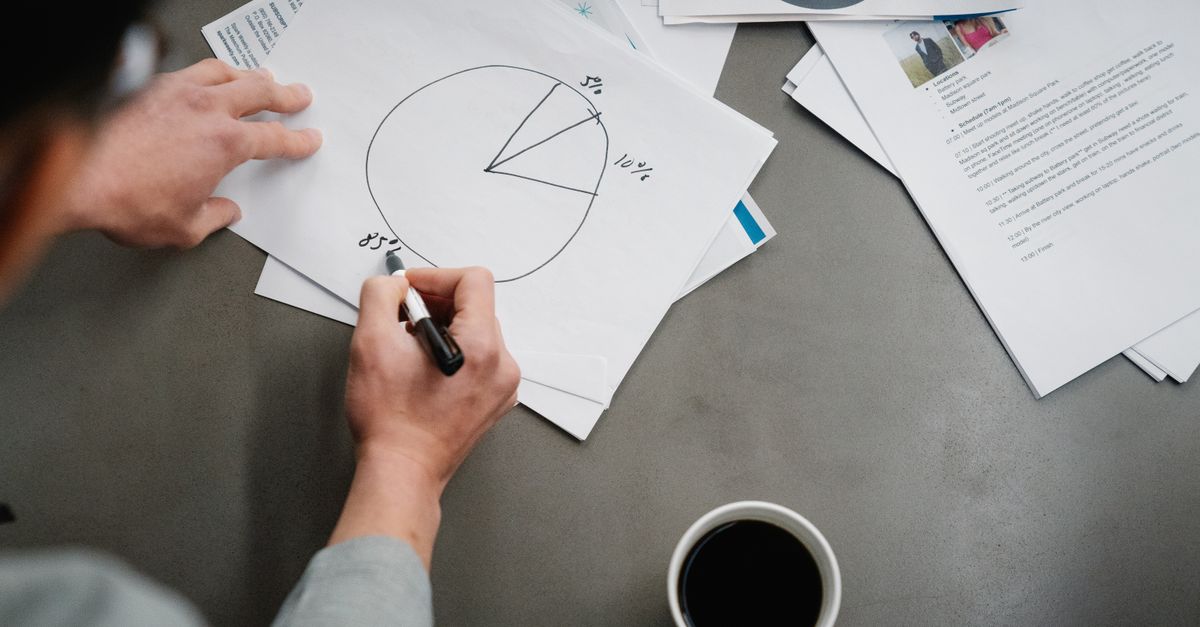 Man drawing a pie chart on paper with coffee, representing business planning and analysis.